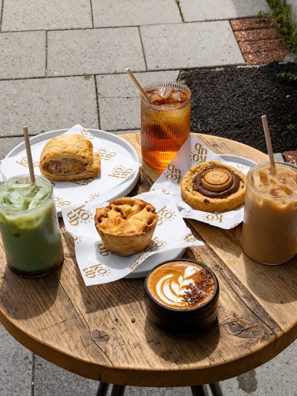 Coffee, matcha and baked treats on a wooden table outside Coffee Koub
